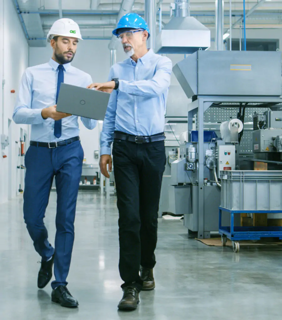 Head of the project holds laptop and discussing details with chief engineer while they walk through modern factory.